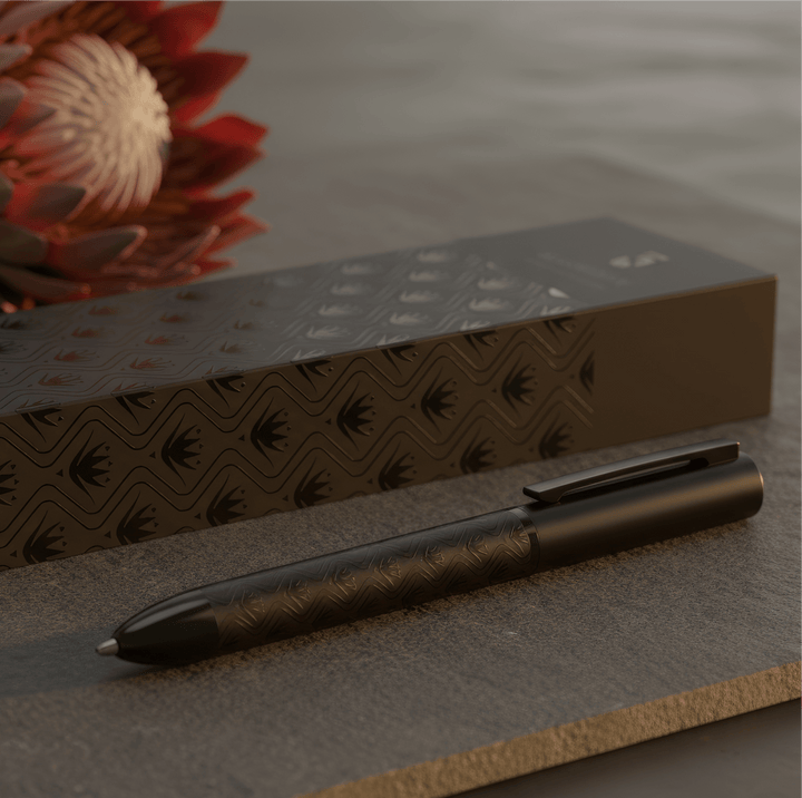 Sengetti Protea Signature Ball Pen from Andy Cartwright Collection on a slate surface with floral background.